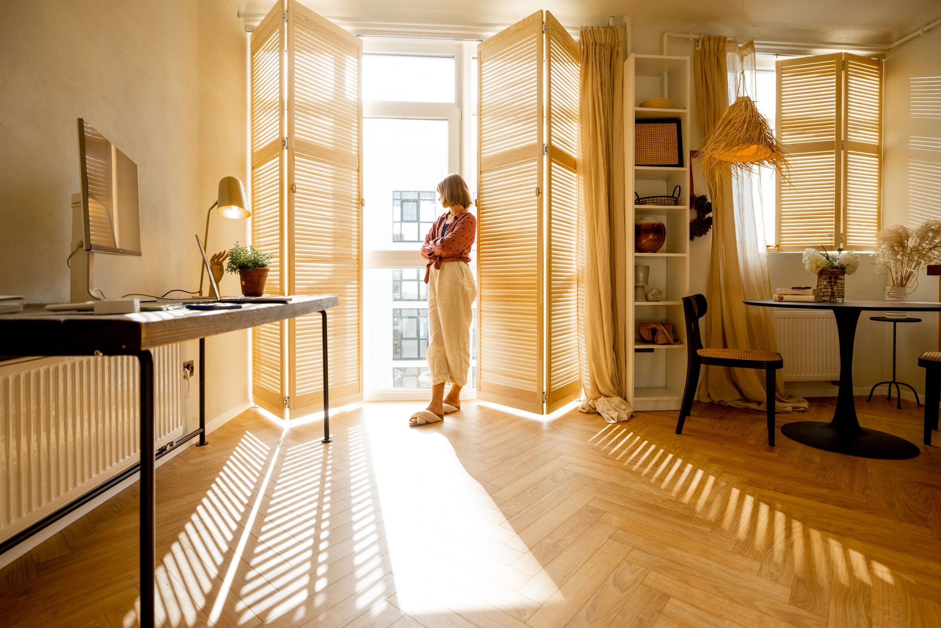 Woman stands alone by the window blinds at home