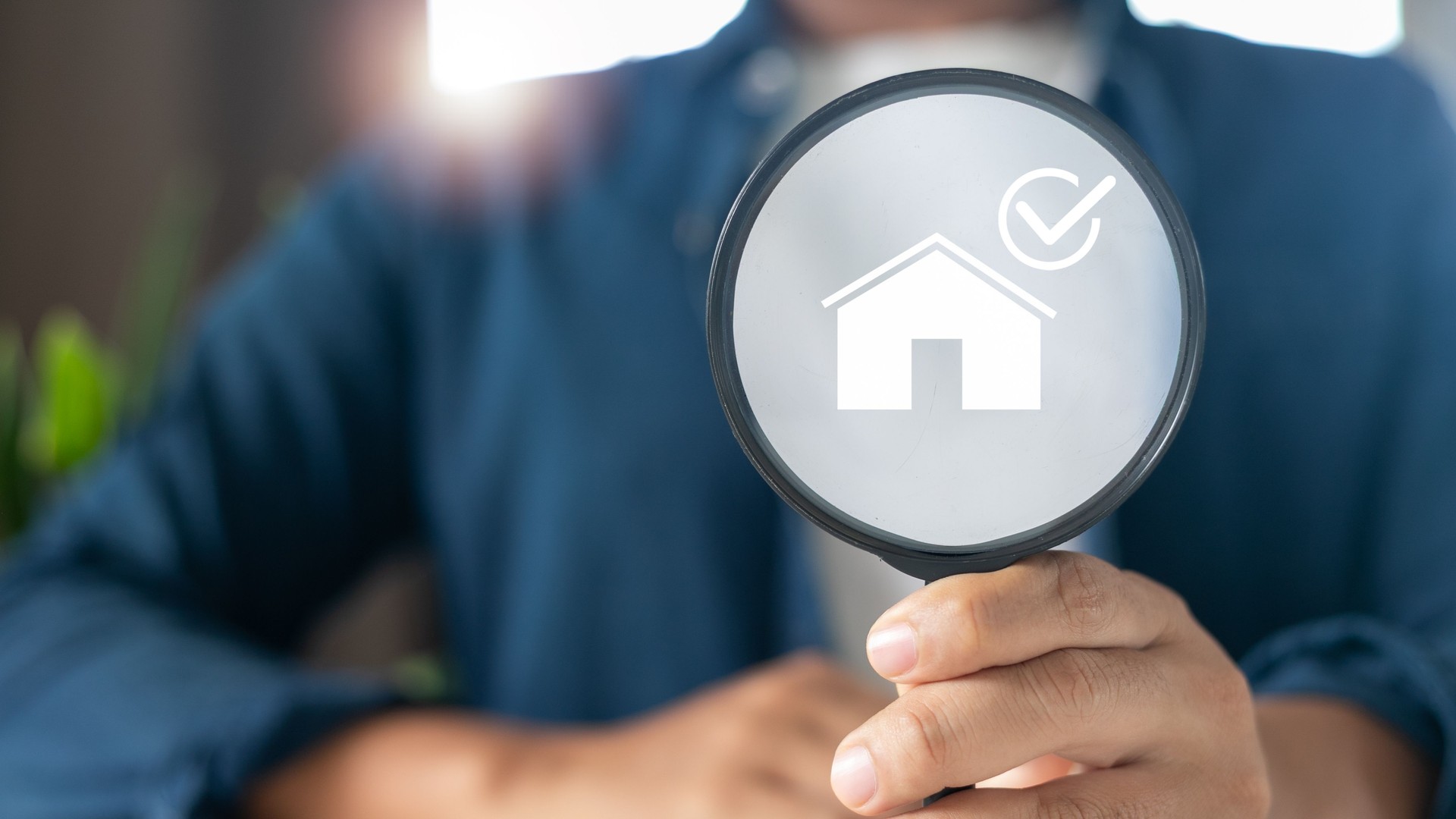 Close-up hand holding magnifying glass with house check mark icon, concept of property inspection, real estate approval, home verification, housing quality control.