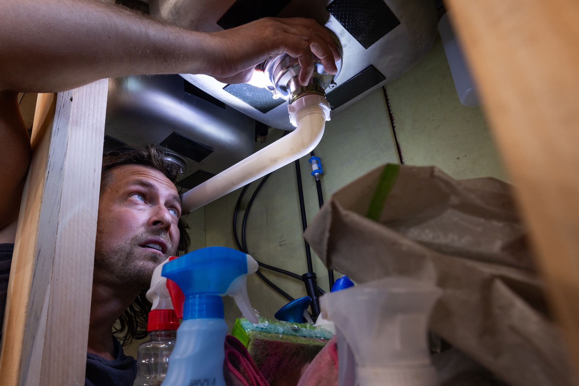 Inspecting Plumbing Under the Kitchen Sink with a Flashlight